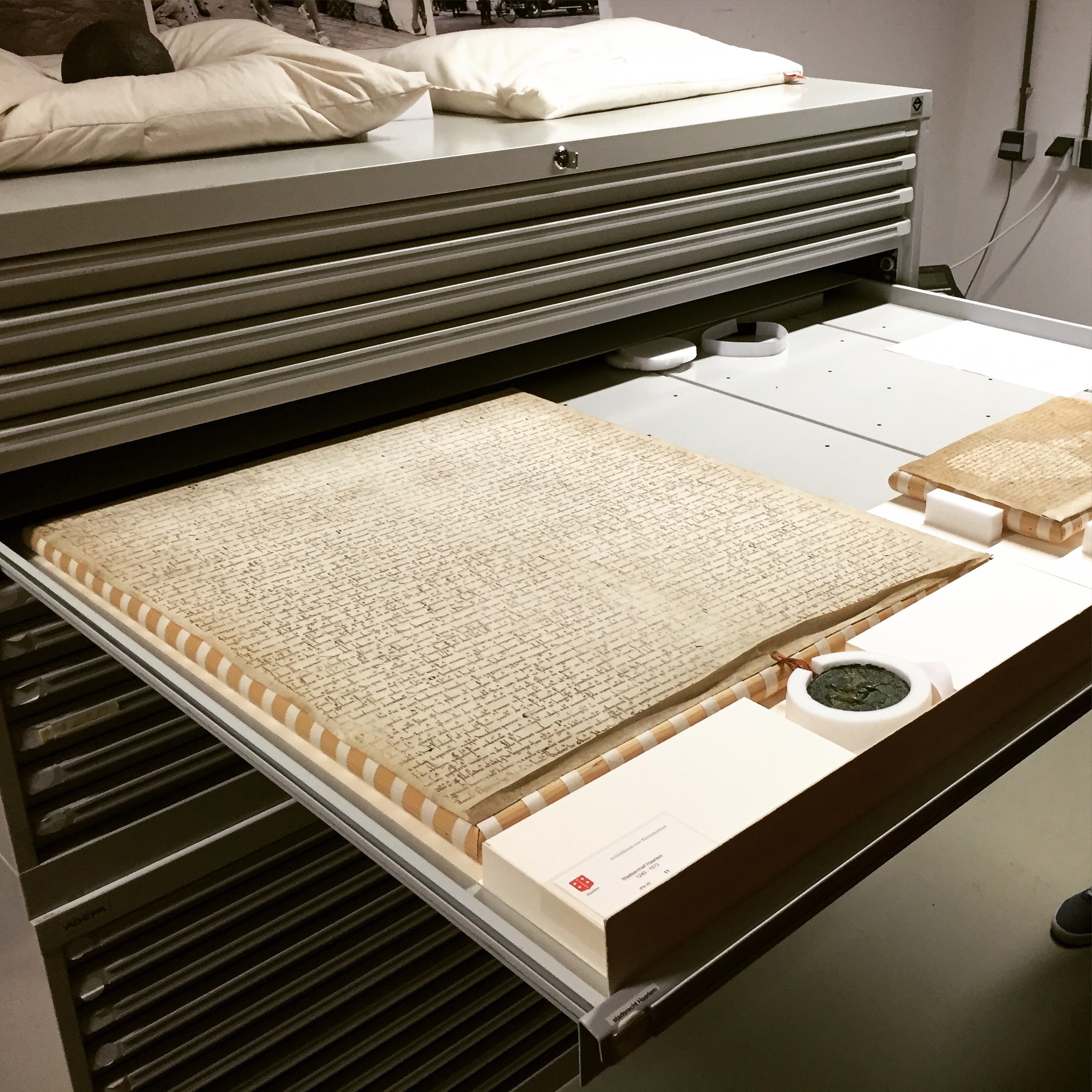 Image for Met het Noord-Hollands archief als nieuwe klant mochten we een kijkje nemen in het depot waar het perkamenten document ligt met de stadswetten van Haarlem. En op dat kussen ligt een kogel.